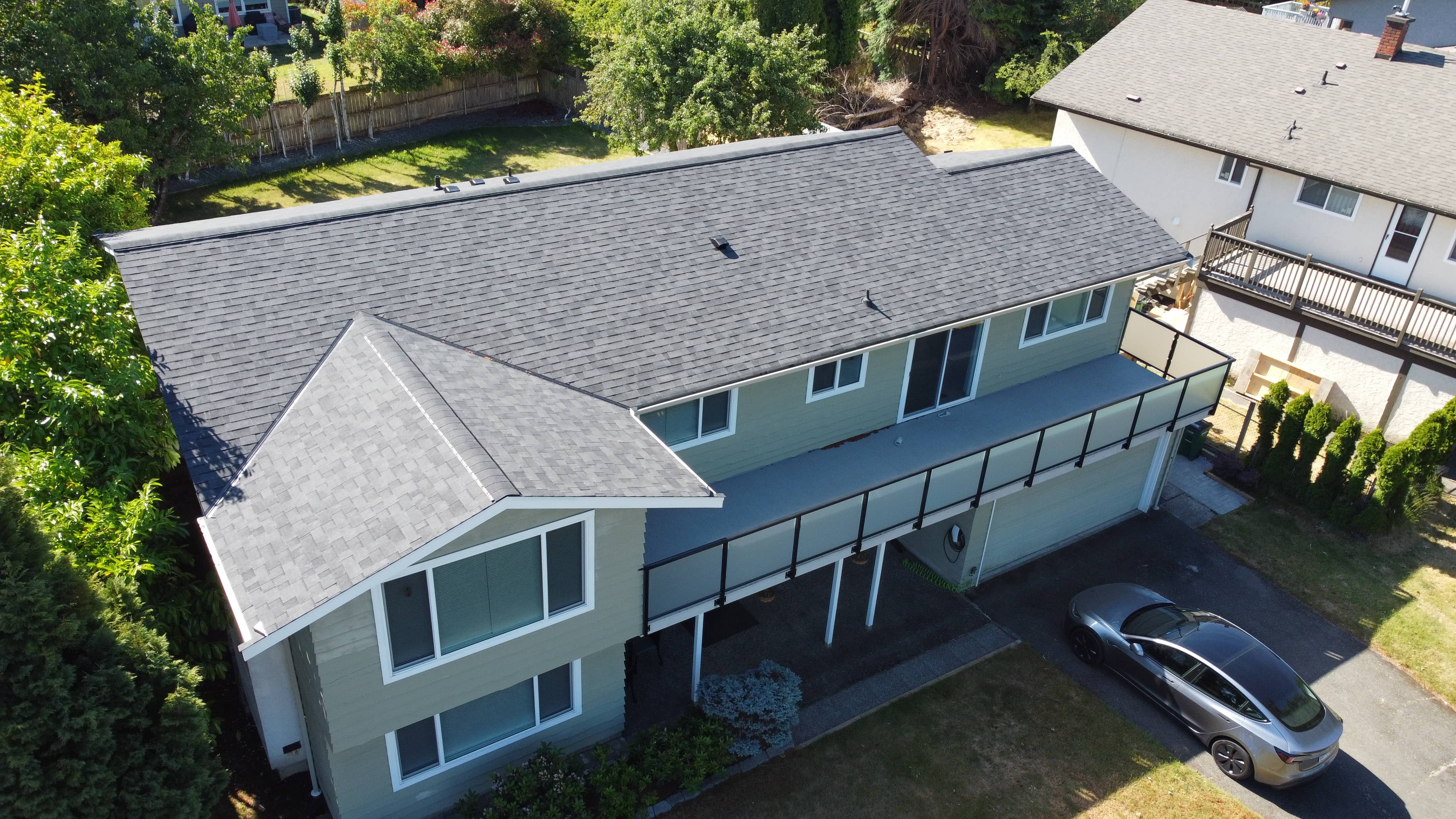 After - new grey asphalt shingle roof on green two-storey home installed by McGuire Roofing